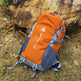 Orange and gray backpack with visible branding on a grassy ground with rocks.