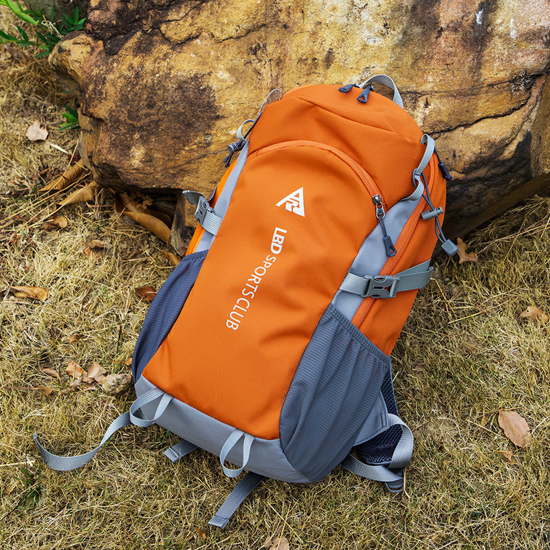 Orange and gray backpack with visible branding on a grassy ground with rocks.