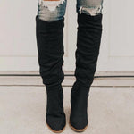 Black knee-high boots worn with ripped jeans on a neutral background