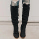 Black knee-high boots worn with ripped jeans on a neutral background