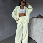 Person wearing a light yellow tracksuit with a white top in a minimalistic setting.