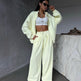 Person wearing a light yellow tracksuit with a white top in a minimalistic setting.