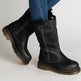 Black leather boots worn with blue jeans on a light gray background