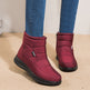 Red winter boots worn with blue jeans on a beige floor.