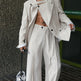 Person wearing a beige suit with a shirtless torso against a textured wall.