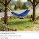 A blue canvas hammock with white tassels hangs between two trees in a garden setting. Product details text is shown at the bottom of the image.