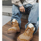 A person seated on concrete steps wearing tan bandana-print lace-up boots with white socks and light blue jeans.