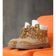 A pair of tan lace-up ankle boots with a white paisley bandana print on the sides, white cuffs, and brown laces, displayed on an orange chair against a dark gray textured background.