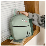 Green dinosaur-shaped backpack held by a hand on a wooden surface.