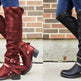 Red and black knee-high boots worn by a person against a brick wall.