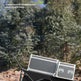 A black and gray wheeled cargo cart with two metal storage cases, shown outdoors on a rocky path with trees in the background. White text in the upper left reads '360° universal wheel' with a subtitle about free control, stopping, and pausing with ease.