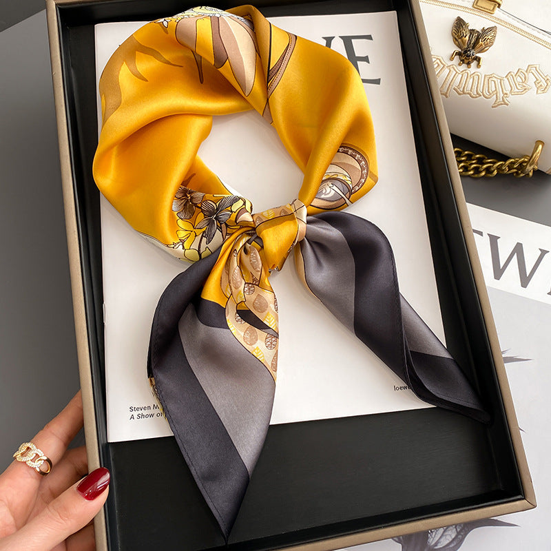 Yellow and black patterned silk scarf in a box with a hand holding it.
