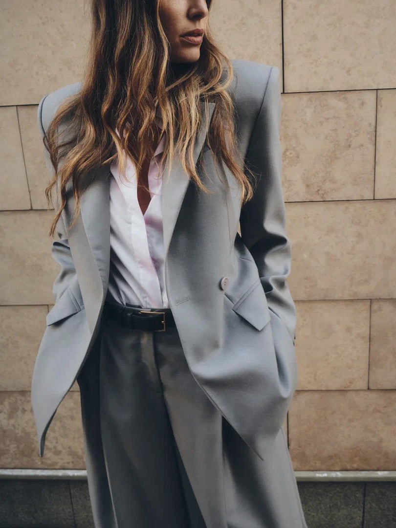 Person wearing a light gray coat against a beige wall.