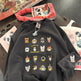Black sweatshirt with cat illustrations on a table with books and sunglasses.