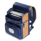 A navy blue and tan school backpack shown open, containing a stack of notebooks or magazines. The backpack features multiple compartments, a front pocket with a clear window, and padded shoulder straps, photographed on a white background.