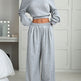 Person wearing a gray off-shoulder top and wide-leg pants in a bedroom setting.