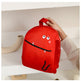 Red backpack with a cartoon face design held by a person on a white surface.