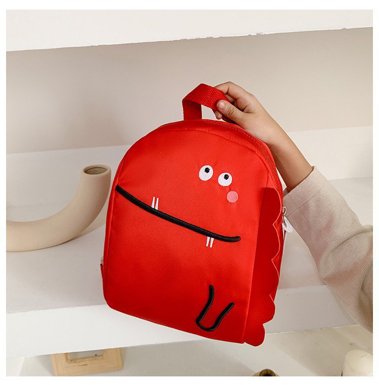 Red backpack with a cartoon face design held by a person on a white surface.