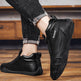 Black slip-on shoes with 'Daap' branding worn by a person on a wooden floor.