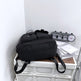 Black backpack on a white surface with a clock and papers in the background