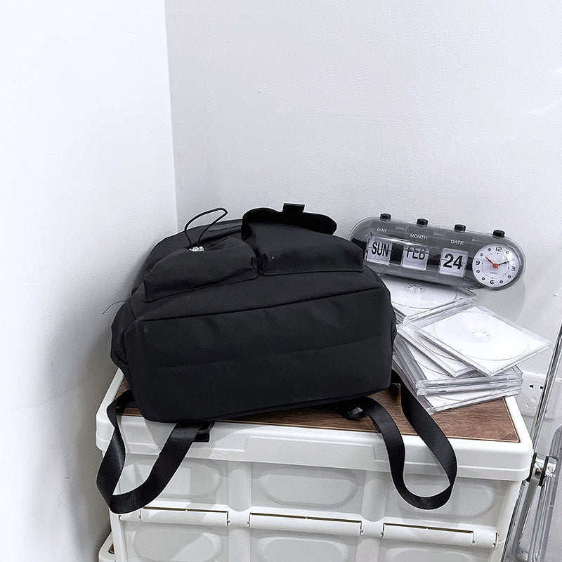 Black backpack on a white surface with a clock and papers in the background