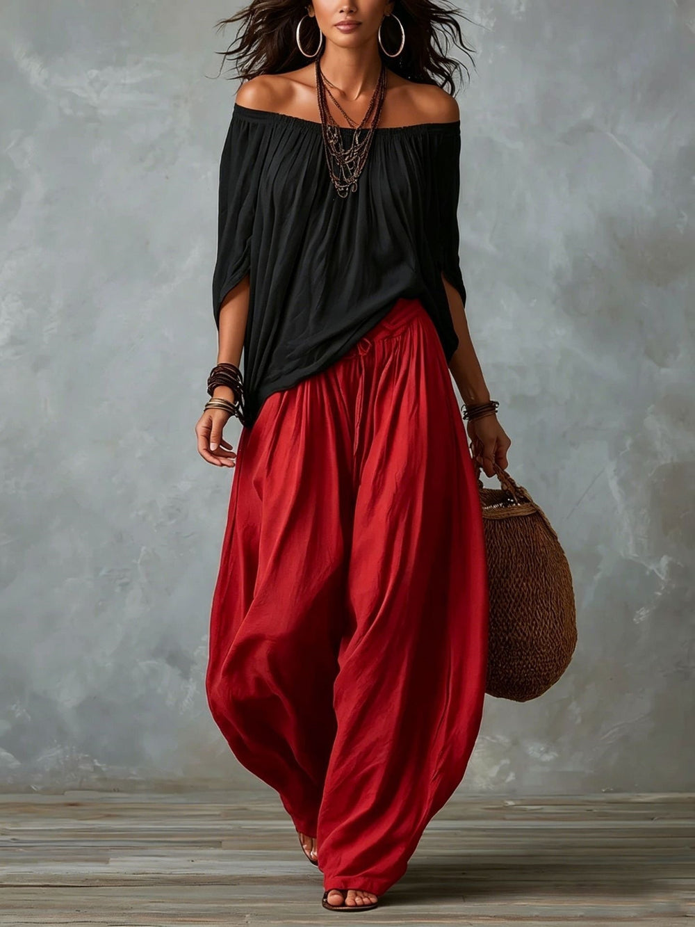 Woman wearing a black off-shoulder top and red harem pants against a gray background