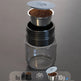 Coffee brewing device with a clear container and metal filter on a gray background