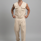 A man modeling a light beige sleeveless utility vest and matching wide-leg trousers set, paired with beige sandals, against a neutral gray studio background.