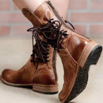 Brown leather boots with laces worn by a person on a light background