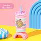 A pink and white striped tumbler cup with a cute bear face graphic, resting on a pink stand. It has a light blue straw and is set against a colorful background with pink and yellow surfaces, blue arches, and a matching cushion.