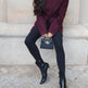 Woman wearing a burgundy coat, black leggings, and black boots sitting on a stone bench.