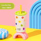 A 12oz plastic cup with a yellow straw, decorated with colorful lime-dot patterns on a white body, resting on a pink arch stand. The background is a bright, playful studio setup with a pink and yellow surface, a blue arch, and a text label reading 'Lime Dot Dot 12oz / 360ml'.