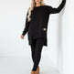 Person wearing a black outfit with beige boots against a white wall.
