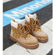 A pair of tan and white bandana-patterned lace-up ankle boots placed on a street crosswalk with a blue sign in the background.