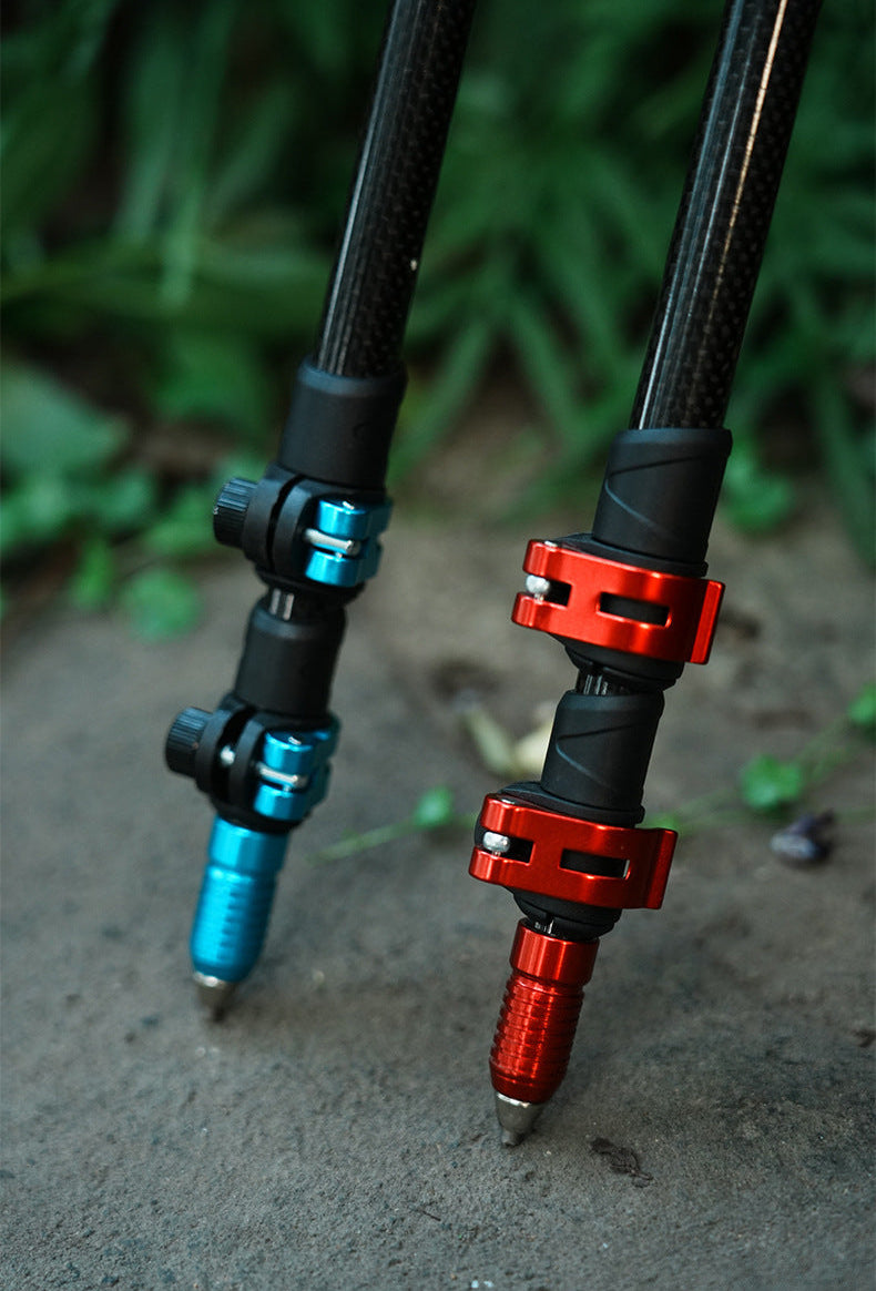 Close-up of two carbon fiber tripod legs with anodized metal couplers, one in blue and one in red, standing on a concrete surface with green foliage blurred in the background.