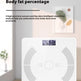 A white digital body fat percentage scale is shown in a bright, modern room setting. The scale features a digital display showing '42.