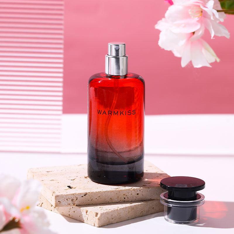 Red perfume bottle labeled 'WARMKISS' on a light surface with a pink background