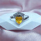 Ring with yellow gemstone and engraved text on a pink fabric background