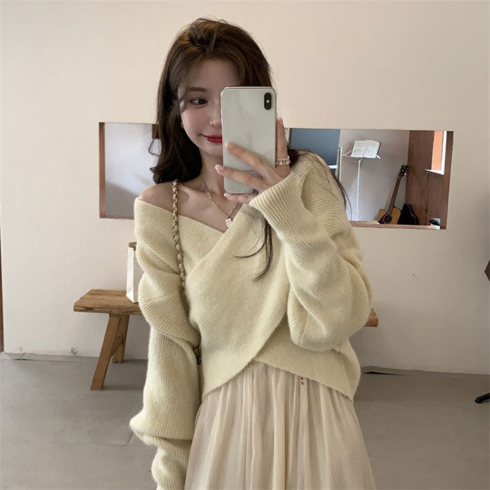 Woman taking a mirror selfie wearing a light-colored sweater and skirt in a minimalistic room.