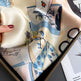Silk scarf with artistic design held over a magazine