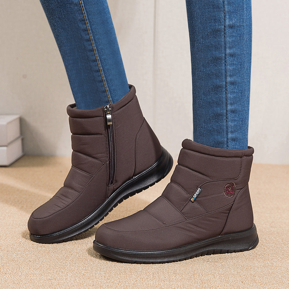 Brown winter boots with zippers worn with blue jeans on a beige surface.