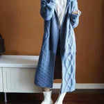 Mannequin wearing a long blue knitted coat against a brown wall.