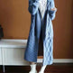 Mannequin wearing a long blue knitted coat against a brown wall.