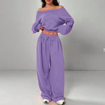Person wearing a purple off-shoulder top and wide-leg pants on a gray background