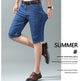 A man modeling blue denim knee-length shorts with a white shirt and brown dress shoes, shown against a light gray studio background with promotional text on the right.