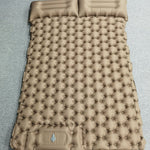 A tan inflatable sleeping pad with a quilted bubble pattern and two integrated headrests, laid flat on a gray textured surface.