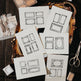 Sheets of decorative paper with ornate frames on a wooden surface with scissors.