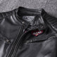 Close-up of a black leather jacket with brand patches on a textured gray background