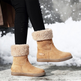 Tan winter boots with fur trim worn by a person on a snowy ground.