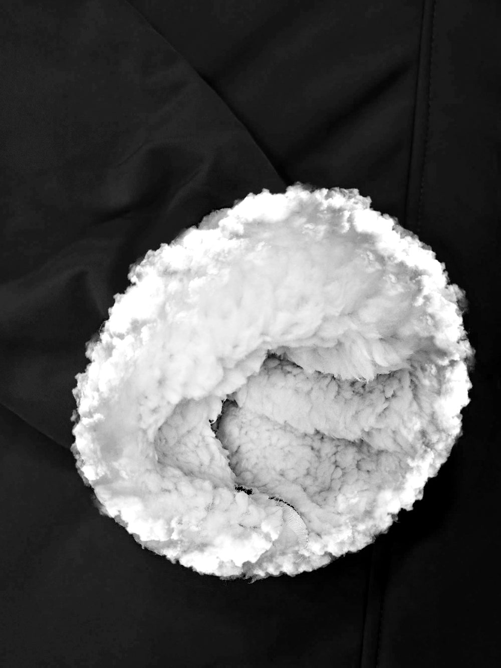 Close-up of a black garment with a large circular opening showing fluffy white faux-fur lining.
